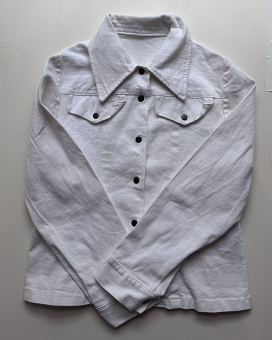 A white long-sleeve button-up shirt with a pointed collar and two buttoned chest flap pockets, laid flat on a light gray background.