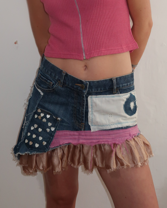 A person wearing an fcuk patchwork denim mini skirt with a pink ruffled hem, a white patch pocket, and a loveheart button denim pocket